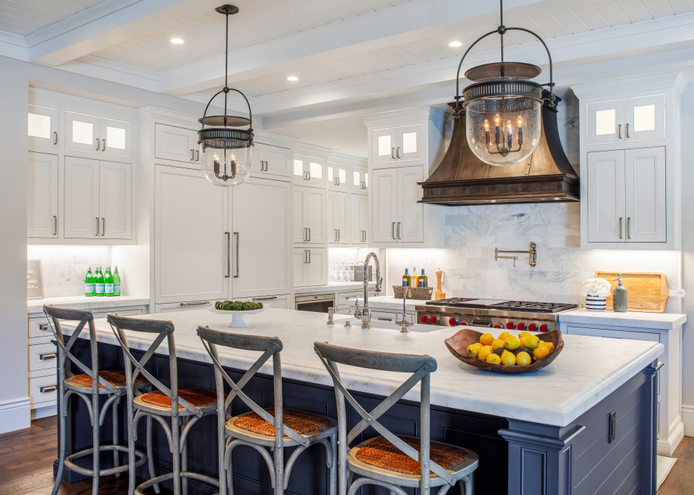 This is an example of an expansive beach style open plan kitchen in San Francisco with a farmhouse sink, beaded inset cabinets, white cabinets, marble benchtops, white splashback, marble splashback, panelled appliances, dark hardwood floors, with island, brown floor, white benchtop and exposed beam.