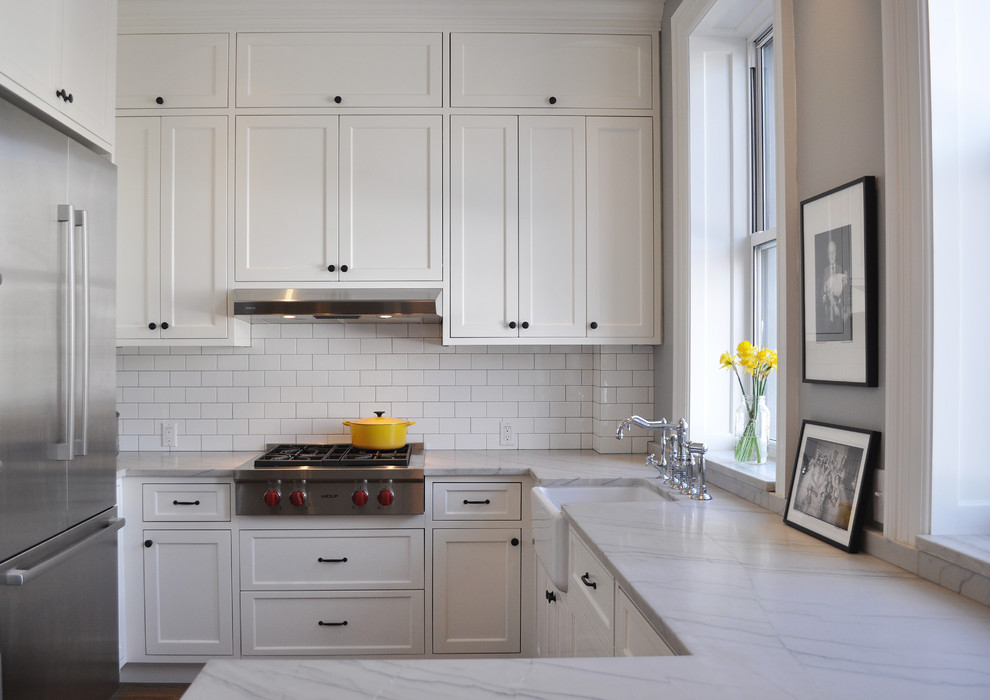 Design ideas for a small transitional u-shaped kitchen in New York with a farmhouse sink, shaker cabinets, white cabinets, white splashback, subway tile splashback, stainless steel appliances and a peninsula.