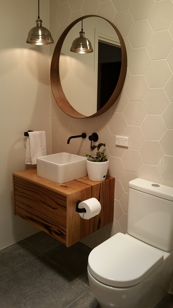 Mid-sized scandinavian master bathroom in Sydney with furniture-like cabinets, medium wood cabinets, a drop-in tub, a shower/bathtub combo, a wall-mount toilet, white tile, ceramic tile, white walls, ceramic floors, a wall-mount sink, wood benchtops and grey floor.