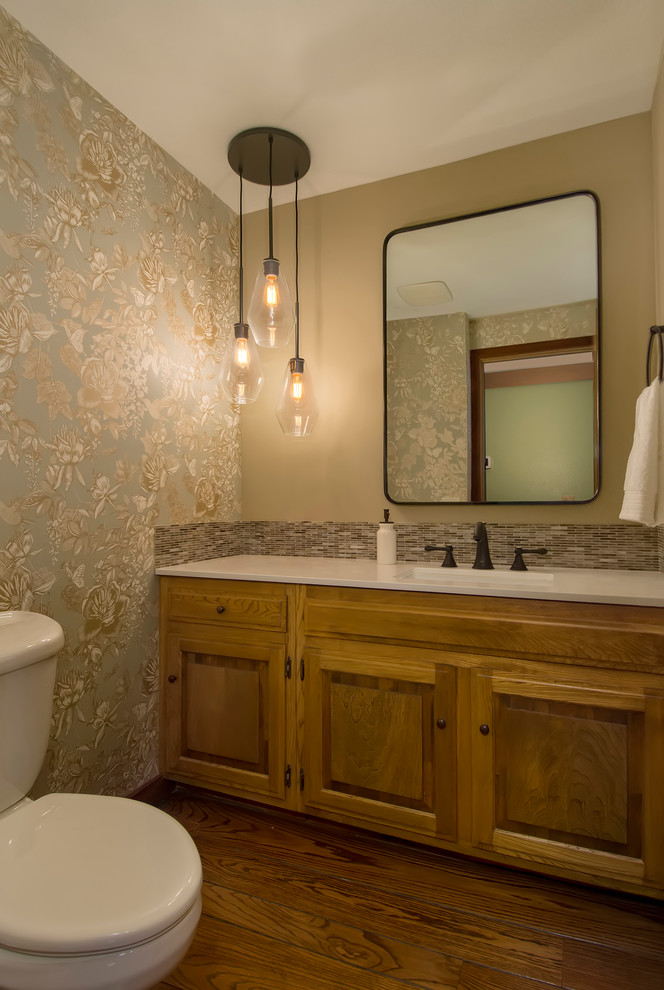 Design ideas for a small transitional powder room in Seattle with raised-panel cabinets, brown cabinets, a wall-mount toilet, multi-coloured tile, glass tile, beige walls, medium hardwood floors, an undermount sink, engineered quartz benchtops, brown floor and white benchtops.