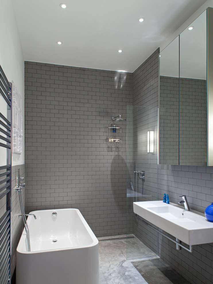 This is an example of a contemporary bathroom in London with a wall-mount sink, a freestanding tub, an open shower, gray tile, subway tile, white walls and an open shower.