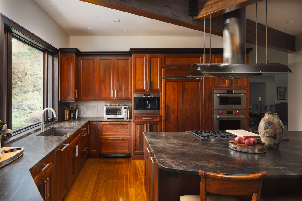 Idéer för ett rustikt svart l-kök, med en undermonterad diskho, luckor med infälld panel, skåp i mörkt trä, bänkskiva i kvartsit, grått stänkskydd, stänkskydd i cementkakel, rostfria vitvaror, mellanmörkt trägolv och en köksö
