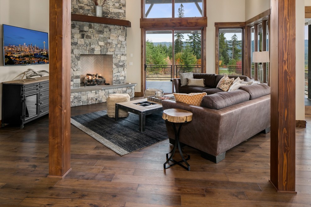 This is an example of a country open concept family room in Seattle with white walls, dark hardwood floors, a standard fireplace, a stone fireplace surround, a wall-mounted tv and brown floor.