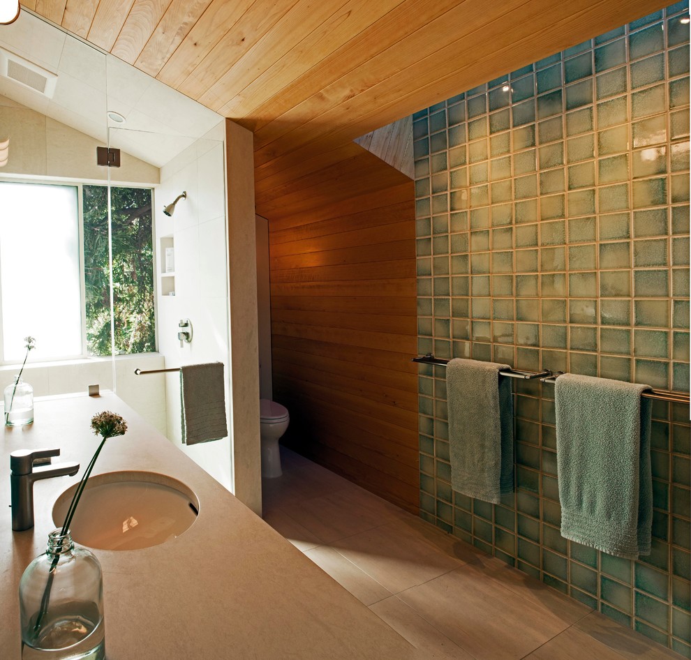 Mid-sized midcentury bathroom in San Francisco with an alcove shower, green tile, an undermount sink, flat-panel cabinets, light wood cabinets, limestone benchtops, a one-piece toilet, ceramic tile, beige walls, porcelain floors and an undermount tub.