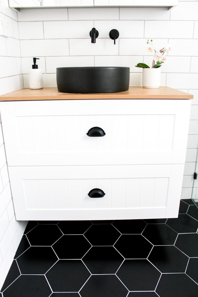 Photo of a small modern kids bathroom in Perth with shaker cabinets, white cabinets, an open shower, a one-piece toilet, white tile, ceramic tile, white walls, porcelain floors, a vessel sink, wood benchtops, black floor, an open shower, beige benchtops, a single vanity, a floating vanity and brick walls.