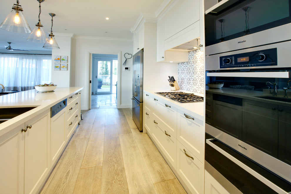 Large beach style single-wall kitchen pantry in Melbourne with a double-bowl sink, beaded inset cabinets, white cabinets, solid surface benchtops, mosaic tile splashback, stainless steel appliances, plywood floors and with island.