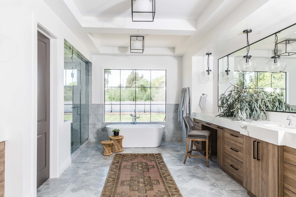 Photo of a country bathroom in Phoenix with flat-panel cabinets, medium wood cabinets, a freestanding tub, an alcove shower, gray tile, white walls, an undermount sink, grey floor, a hinged shower door and white benchtops.