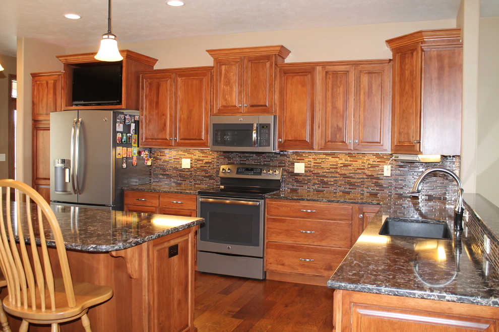Eat-in kitchen - large l-shaped eat-in kitchen idea with an undermount sink, raised-panel cabinets, medium tone wood cabinets, solid surface countertops, glass tile backsplash, stainless steel appliances, beige walls and an island