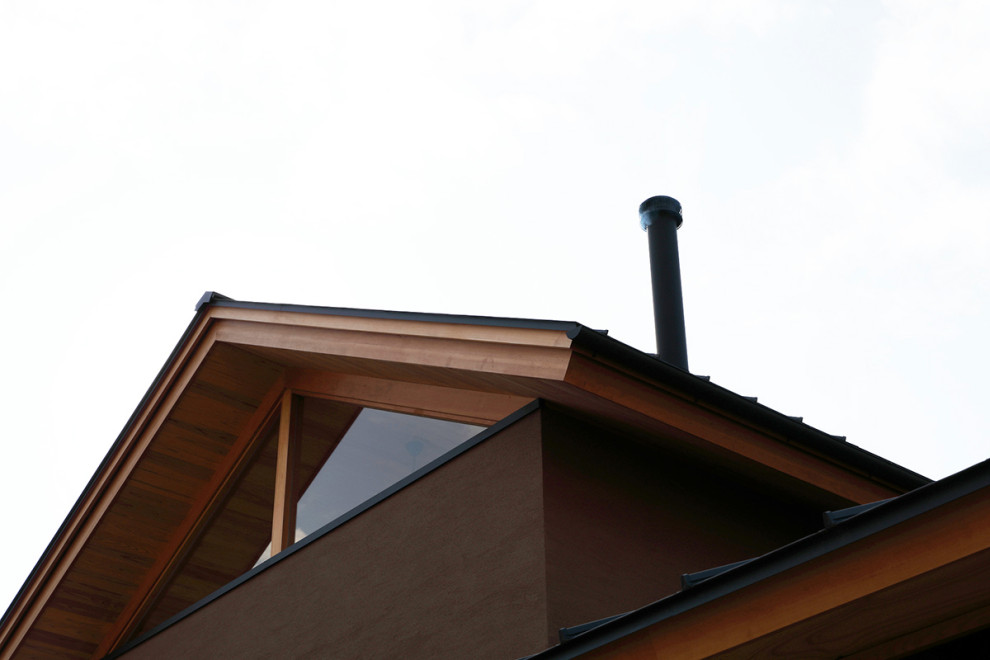 Cette image montre une grande façade de maison marron asiatique en bois et planches et couvre-joints à un étage avec un toit à deux pans, un toit en métal et un toit noir.