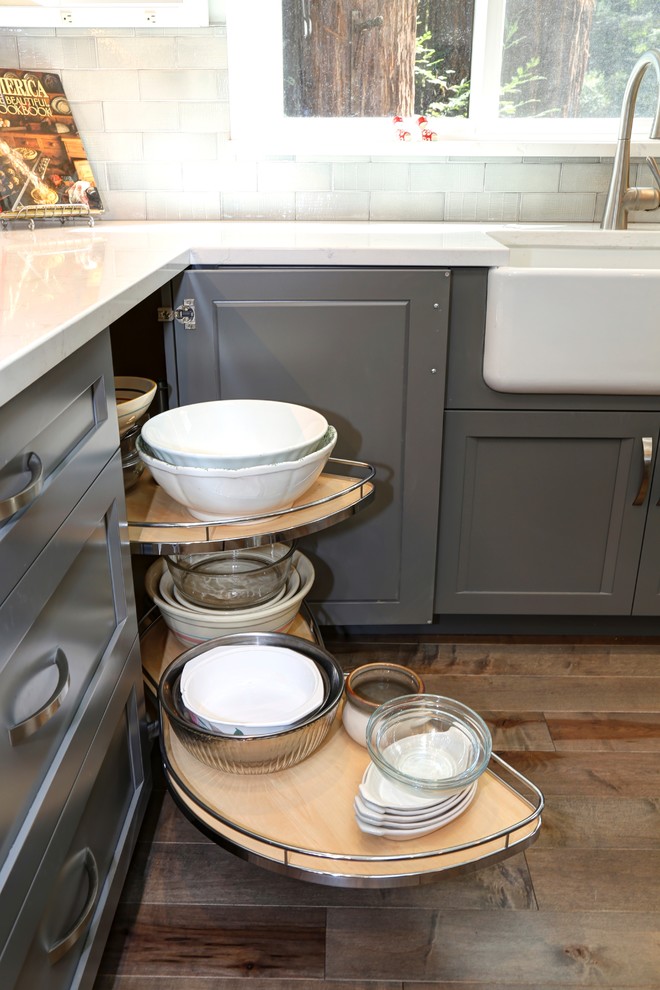 Mid-sized transitional u-shaped medium tone wood floor open concept kitchen photo with a farmhouse sink, raised-panel cabinets, white cabinets, quartz countertops, gray backsplash, subway tile backsplash, stainless steel appliances and an island