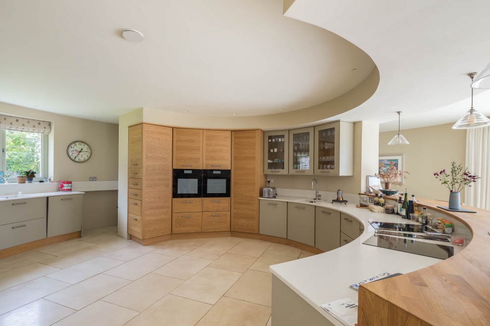 This is an example of a large contemporary kitchen/diner in Cornwall with a built-in sink, flat-panel cabinets, medium wood cabinets, beige splashback, black appliances, limestone flooring, beige floors and beige worktops.