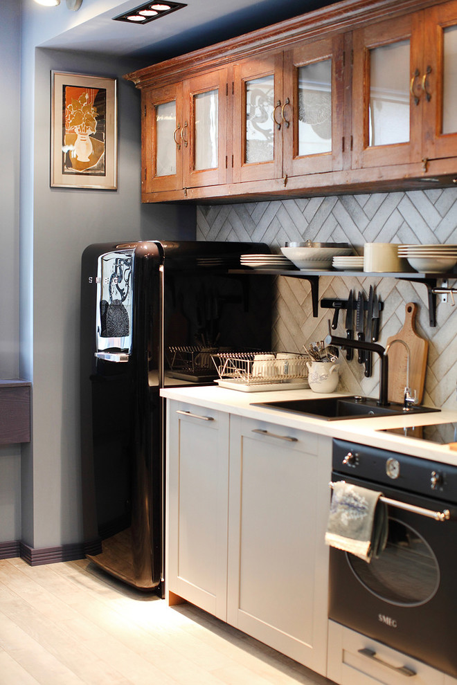 Small eclectic single-wall open plan kitchen in Saint Petersburg with a drop-in sink, grey cabinets, grey splashback, black appliances and light hardwood floors.