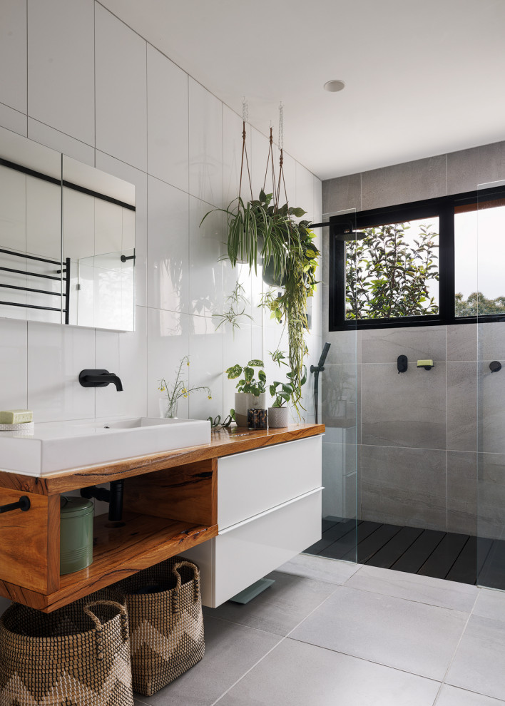 Inspiration for a mid-sized contemporary bathroom in Melbourne with open cabinets, white cabinets, a drop-in tub, a double shower, a one-piece toilet, white tile, white walls, porcelain floors, a wall-mount sink, wood benchtops, grey floor, an open shower, a single vanity and a floating vanity.