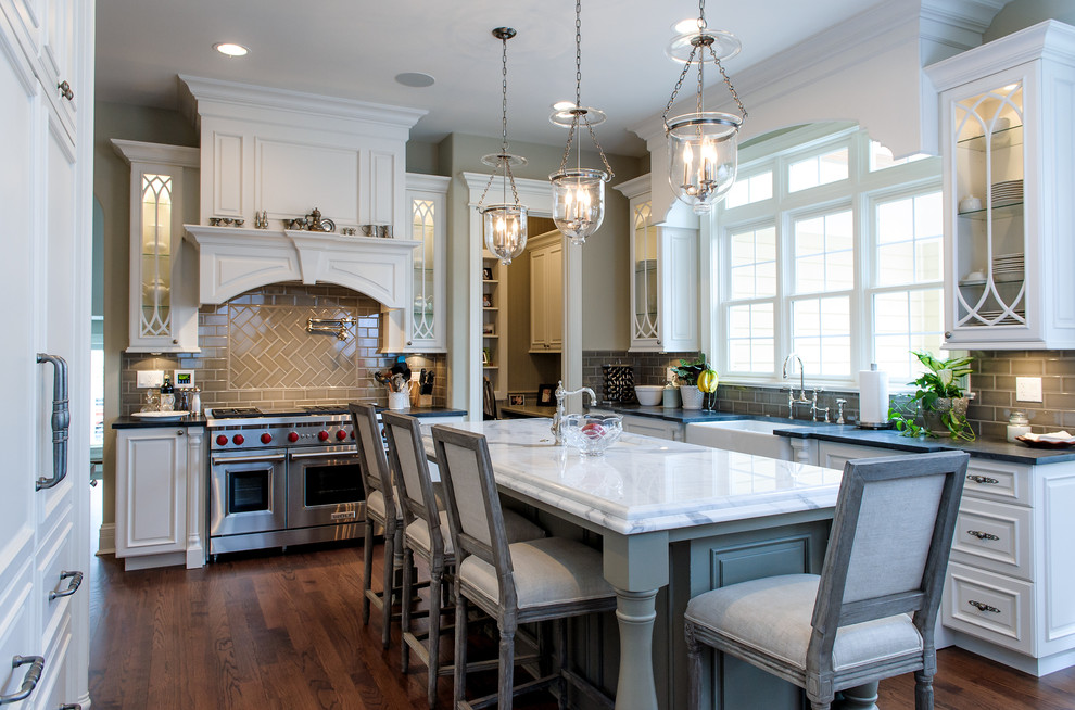 Elegant u-shaped dark wood floor kitchen photo in Chicago with a farmhouse sink, raised-panel cabinets, white cabinets, gray backsplash, subway tile backsplash, stainless steel appliances and an island