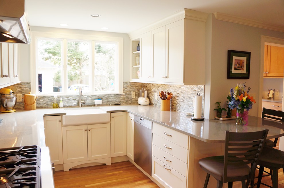 Example of a mid-sized transitional l-shaped light wood floor eat-in kitchen design in Boston with a farmhouse sink, shaker cabinets, white cabinets, quartz countertops, blue backsplash, glass tile backsplash, paneled appliances and a peninsula