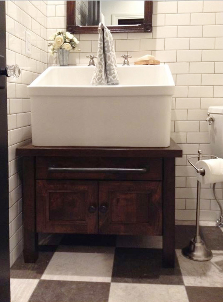 Mid-sized country powder room in Orange County with furniture-like cabinets, medium wood cabinets, a two-piece toilet, white tile, subway tile, white walls, ceramic floors, a vessel sink and multi-coloured floor.