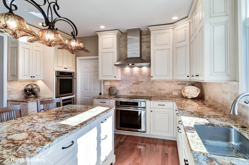 Inspiration for a mid-sized traditional l-shaped eat-in kitchen in Philadelphia with an undermount sink, raised-panel cabinets, white cabinets, granite benchtops, beige splashback, stone tile splashback, stainless steel appliances, medium hardwood floors and with island.