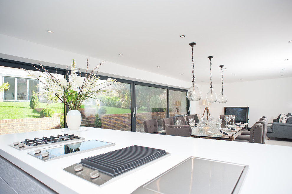 This is an example of a mid-sized modern galley eat-in kitchen in London with an integrated sink, flat-panel cabinets, grey cabinets, laminate benchtops, grey splashback, glass sheet splashback, stainless steel appliances and with island.