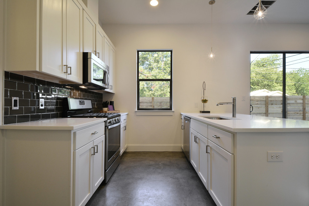 Kitchen - modern galley concrete floor kitchen idea in Austin with white cabinets, quartz countertops, black backsplash, subway tile backsplash and stainless steel appliances