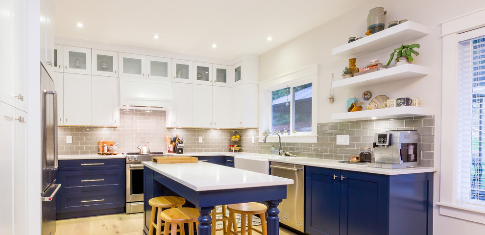 Example of a large transitional u-shaped light wood floor open concept kitchen design with a farmhouse sink, shaker cabinets, blue cabinets, quartz countertops, gray backsplash, glass tile backsplash, stainless steel appliances, an island and white countertops