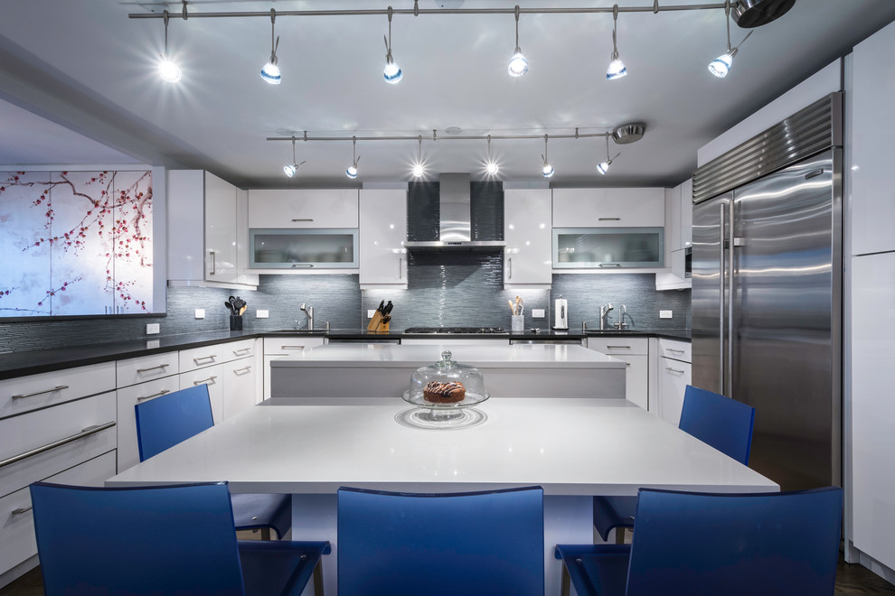 Photo of a mid-sized contemporary u-shaped eat-in kitchen in New York with flat-panel cabinets, white cabinets, grey splashback, with island, glass tile splashback, stainless steel appliances and dark hardwood floors.