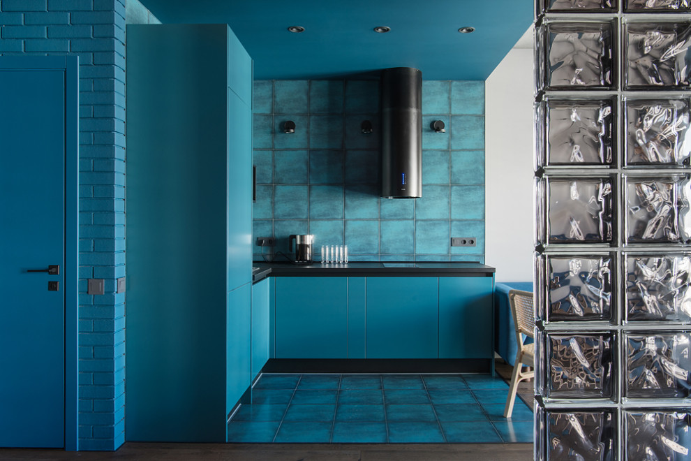 Стильный дизайн: угловая кухня-гостиная среднего размера в стиле лофт с врезной мойкой, плоскими фасадами, синими фасадами, столешницей из ламината, синим фартуком, фартуком из керамической плитки, черной техникой, полом из керамической плитки, синим полом, черной столешницей, многоуровневым потолком и акцентной стеной без острова - последний тренд
