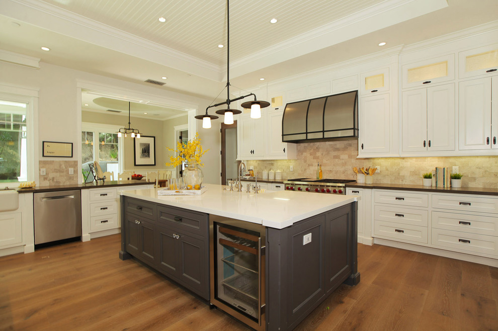 Design ideas for a large country u-shaped open plan kitchen in Los Angeles with a farmhouse sink, shaker cabinets, white cabinets, solid surface benchtops, brown splashback, terra-cotta splashback, stainless steel appliances, medium hardwood floors and multiple islands.