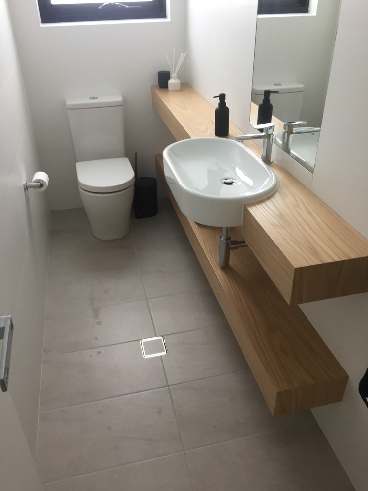 This is an example of a mid-sized contemporary powder room in Sydney with a one-piece toilet, white walls, ceramic floors, a vessel sink, laminate benchtops and grey floor.