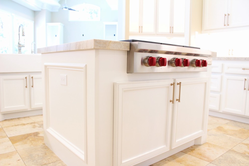 Photo of a large transitional u-shaped eat-in kitchen in Houston with a farmhouse sink, recessed-panel cabinets, white cabinets, quartzite benchtops, beige splashback, limestone splashback, stainless steel appliances, travertine floors, multiple islands and beige floor.