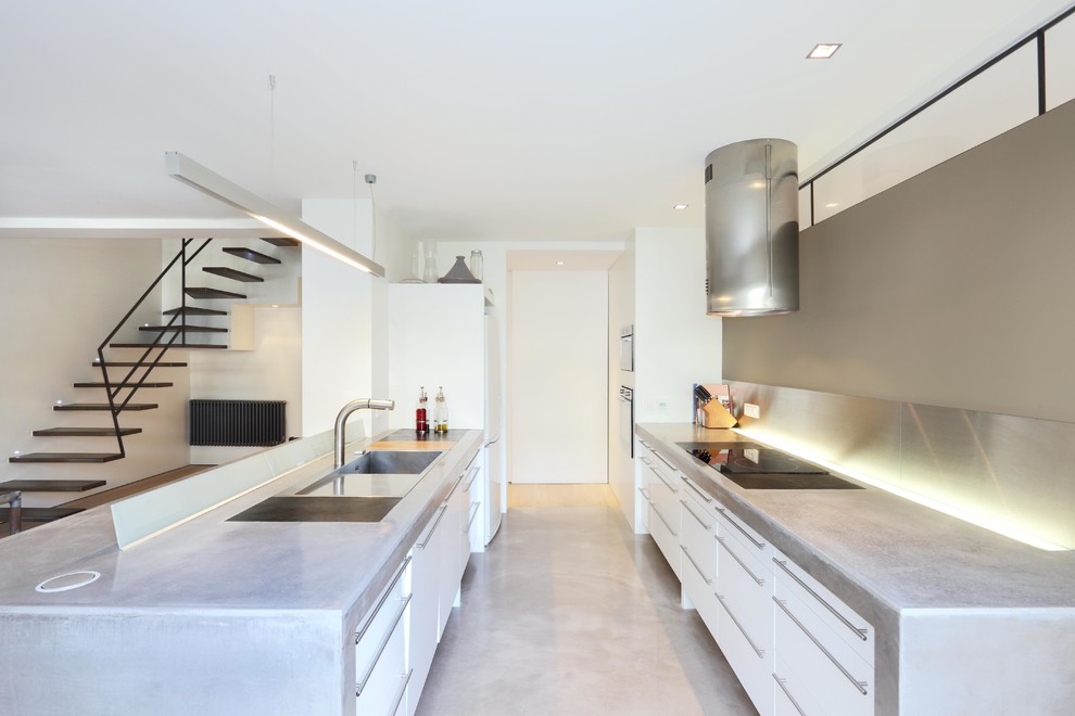 Design ideas for a large contemporary galley open plan kitchen in Paris with concrete benchtops, metal splashback, stainless steel appliances, concrete floors, a drop-in sink, flat-panel cabinets, white cabinets, metallic splashback and with island.
