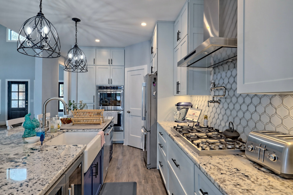 Inspiration for a large transitional l-shaped open plan kitchen in Atlanta with a farmhouse sink, shaker cabinets, grey cabinets, granite benchtops, white splashback, glass tile splashback, stainless steel appliances, vinyl floors, with island, grey floor and multi-coloured benchtop.