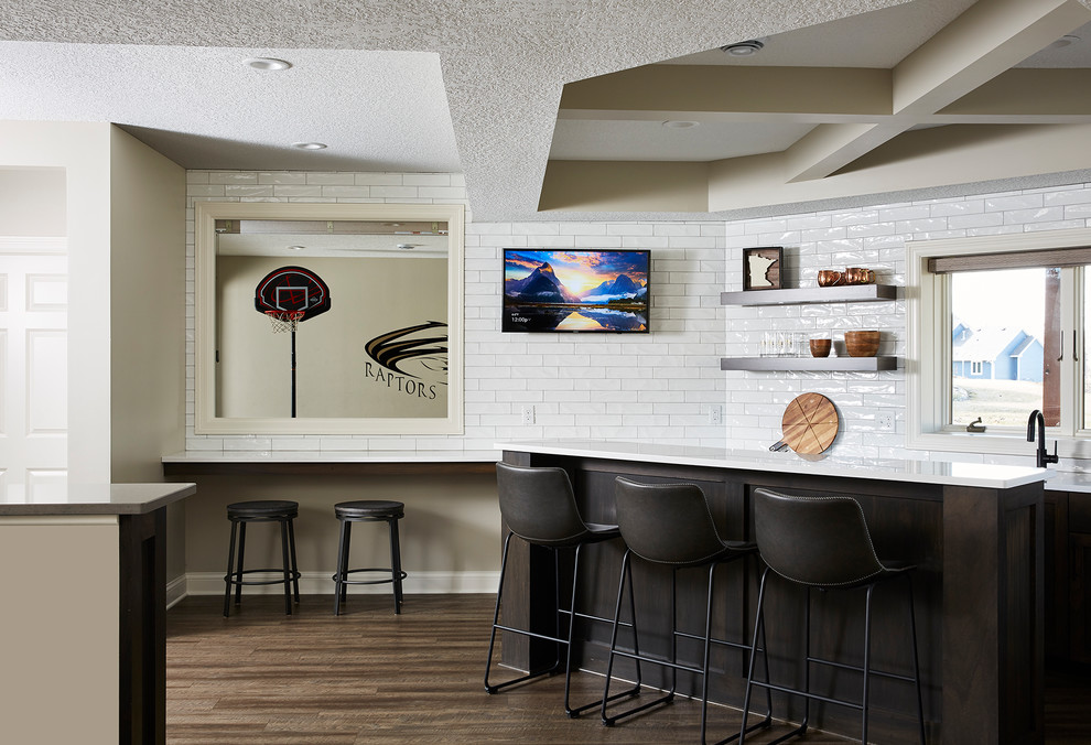 Photo of a mid-sized transitional galley wet bar in Minneapolis with an undermount sink, recessed-panel cabinets, dark wood cabinets, quartz benchtops, white splashback, subway tile splashback, vinyl floors, brown floor and white benchtop.