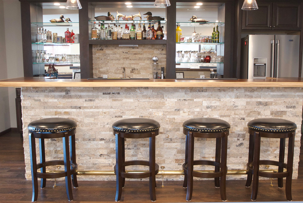 Inspiration for a rustic medium tone wood floor and beige floor home bar remodel with dark wood cabinets, wood countertops, beige backsplash and stone tile backsplash