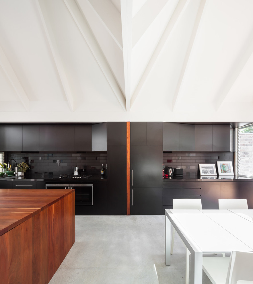 This is an example of a large contemporary kitchen in Sydney with flat-panel cabinets, black cabinets, black splashback and concrete floors.