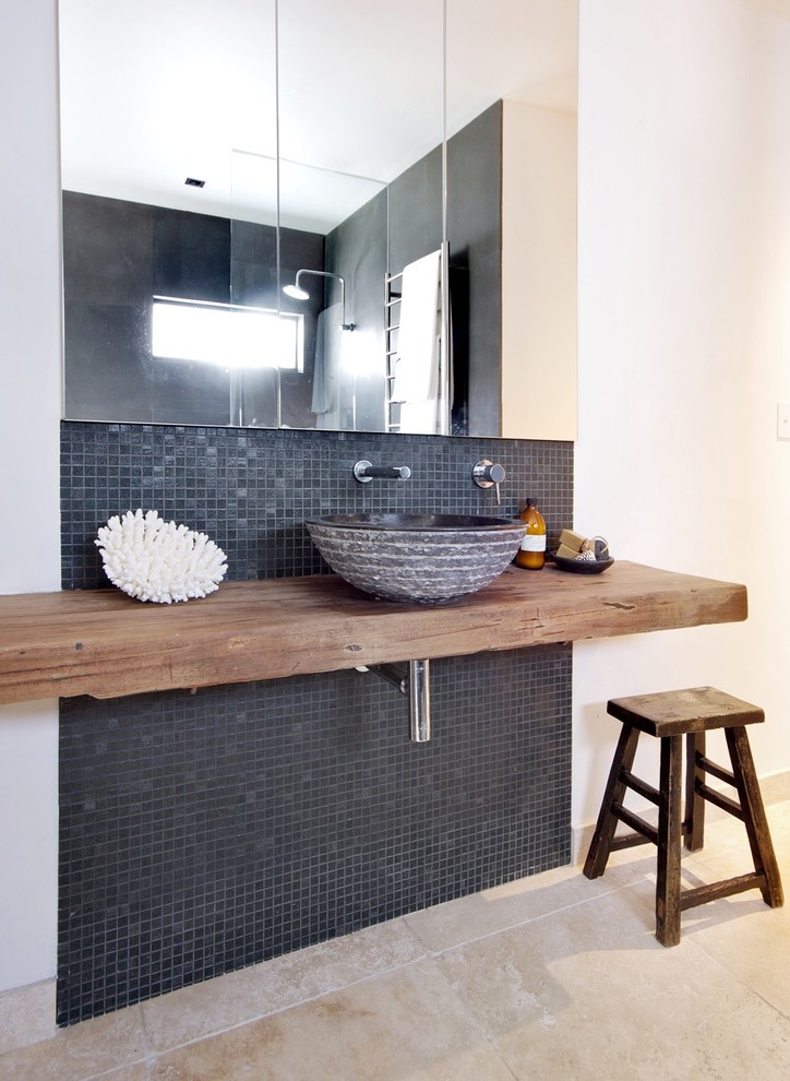This is an example of a mid-sized eclectic master bathroom in Sydney with open cabinets, light wood cabinets, a drop-in tub, an open shower, a wall-mount toilet, black tile, porcelain tile, white walls, travertine floors, a vessel sink and wood benchtops.
