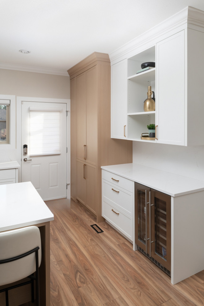 Large u-shaped medium tone wood floor kitchen photo with an undermount sink, shaker cabinets, white cabinets, quartzite countertops, white backsplash, an island and white countertops