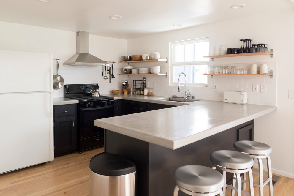 This is an example of a mid-sized contemporary l-shaped open plan kitchen in San Francisco with an undermount sink, shaker cabinets, black cabinets, concrete benchtops, white splashback, subway tile splashback, stainless steel appliances, light hardwood floors, a peninsula, brown floor and grey benchtop.