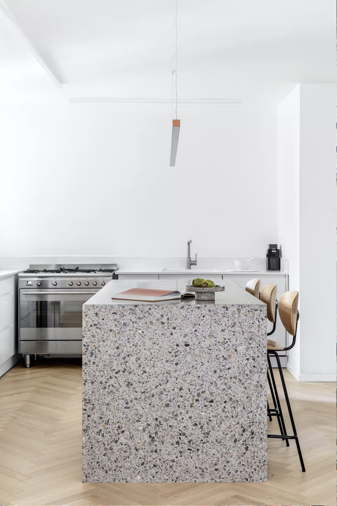 This is an example of a mid-sized single-wall eat-in kitchen in Los Angeles with a drop-in sink, flat-panel cabinets, white cabinets, terrazzo benchtops, white splashback, ceramic splashback, stainless steel appliances, plywood floors, with island, beige floor and white benchtop.