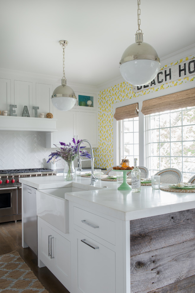 Beach style kitchen in New York with a farmhouse sink, shaker cabinets, white cabinets, white splashback, stainless steel appliances and with island.