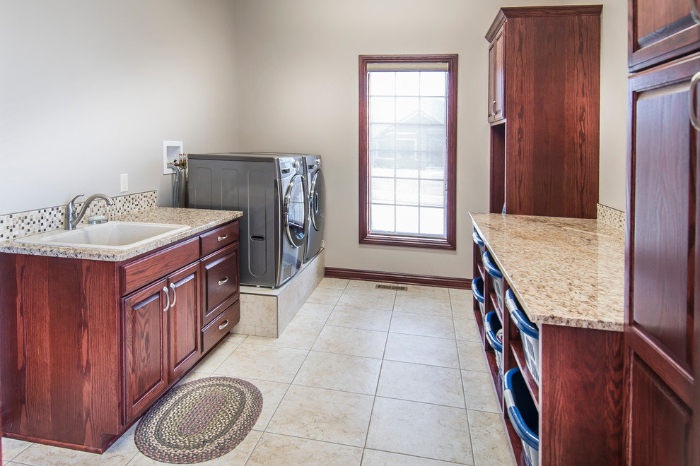 Design ideas for a mid-sized transitional galley dedicated laundry room in Omaha with a single-bowl sink, raised-panel cabinets, dark wood cabinets, granite benchtops, beige walls, ceramic floors and a side-by-side washer and dryer.
