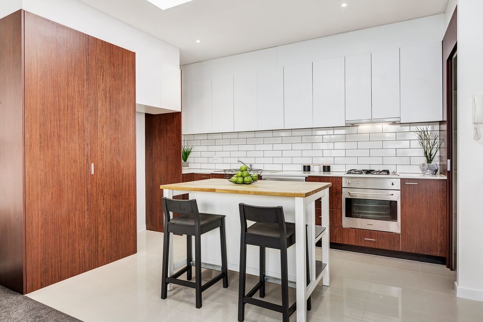 Inspiration for a transitional single-wall kitchen in Melbourne with flat-panel cabinets, brown cabinets, white splashback, subway tile splashback, stainless steel appliances, with island and white floor.