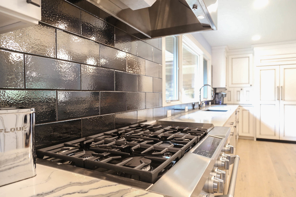 Example of a mid-sized transitional u-shaped light wood floor and beige floor eat-in kitchen design with an undermount sink, recessed-panel cabinets, white cabinets, quartzite countertops, black backsplash, porcelain backsplash, stainless steel appliances, an island and white countertops
