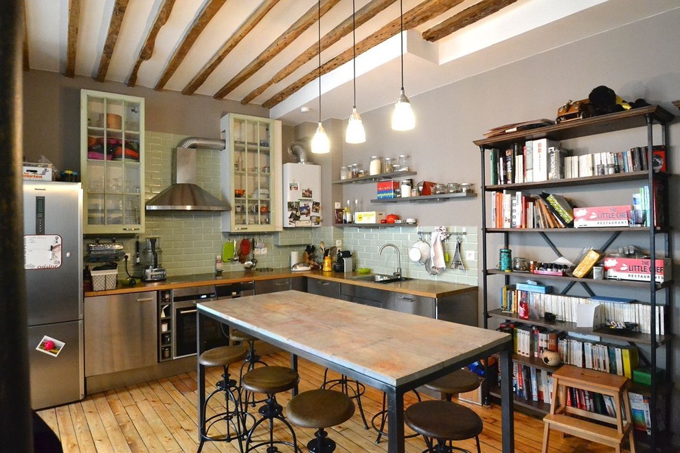 Mid-sized industrial l-shaped open plan kitchen in Paris with an undermount sink, stainless steel cabinets, wood benchtops, green splashback, subway tile splashback, stainless steel appliances and medium hardwood floors.