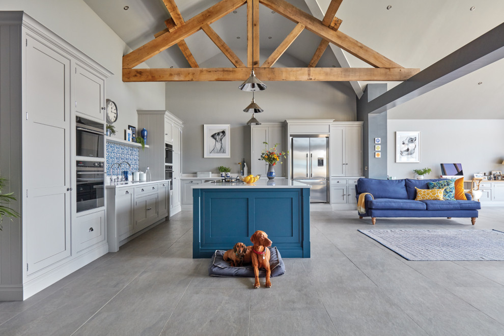 Large contemporary l-shaped open plan kitchen with an integrated sink, shaker cabinets, grey cabinets, quartz worktops, blue splashback, stone tiled splashback, stainless steel appliances, porcelain flooring, an island, grey floors and white worktops.