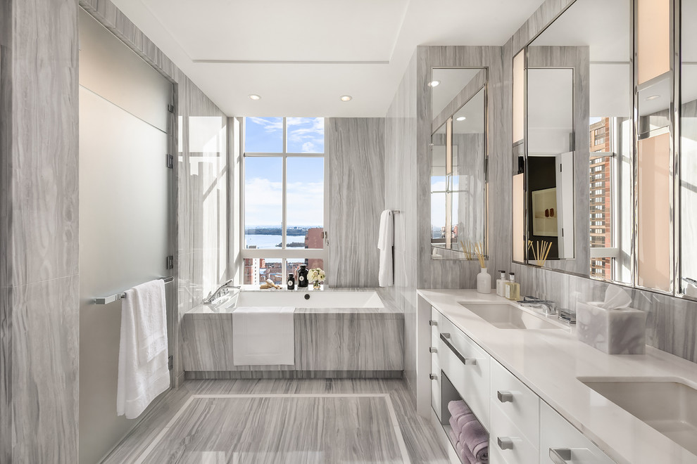 Photo of a large contemporary master bathroom in New York with flat-panel cabinets, white cabinets, an alcove tub, gray tile, grey walls, porcelain floors, an undermount sink, solid surface benchtops, grey floor and white benchtops.