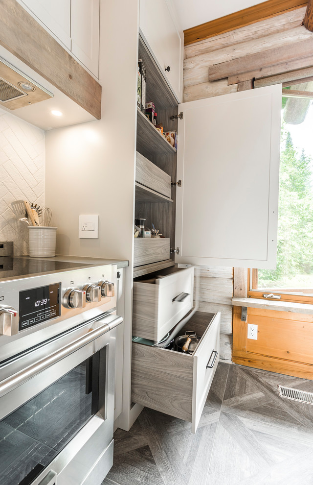 This is an example of a large country u-shaped eat-in kitchen in Montreal with an undermount sink, shaker cabinets, concrete benchtops, white splashback, panelled appliances, porcelain floors, with island, grey floor, grey benchtop, white cabinets and ceramic splashback.