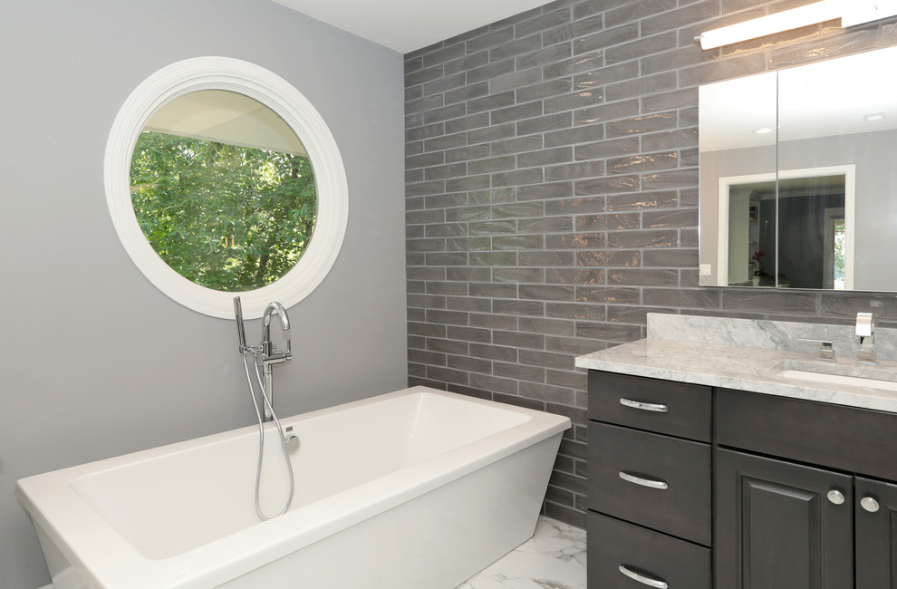 Large transitional master subway tile porcelain tile and white floor freestanding bathtub photo with raised-panel cabinets, gray cabinets, gray walls, an undermount sink and granite countertops