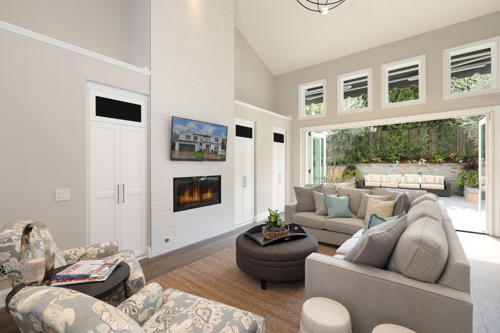 This is an example of a mid-sized transitional open concept family room in Orange County with grey walls, medium hardwood floors, a standard fireplace, a tile fireplace surround, a wall-mounted tv, brown floor and vaulted.