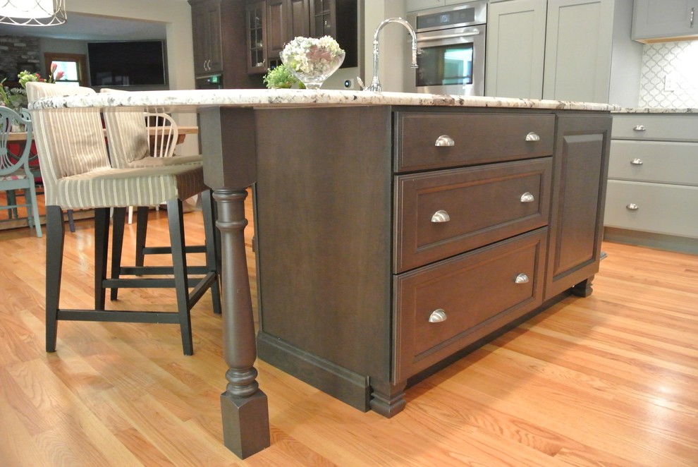 Inspiration for a large transitional l-shaped light wood floor eat-in kitchen remodel in Boston with a farmhouse sink, shaker cabinets, gray cabinets, granite countertops, white backsplash, ceramic backsplash, stainless steel appliances, an island and gray countertops