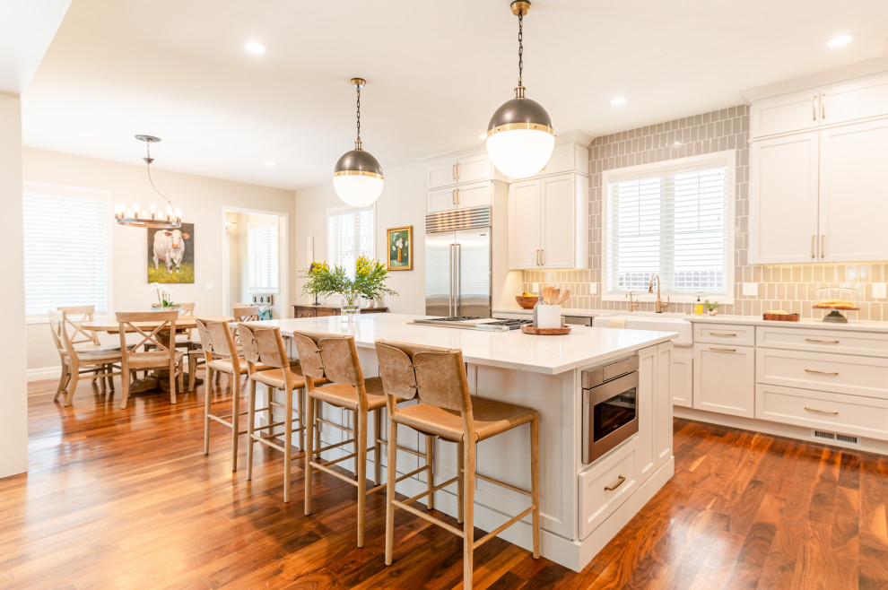 Example of a large transitional l-shaped dark wood floor and brown floor open concept kitchen design in Denver with a farmhouse sink, shaker cabinets, beige cabinets, quartz countertops, beige backsplash, ceramic backsplash, stainless steel appliances, an island and white countertops
